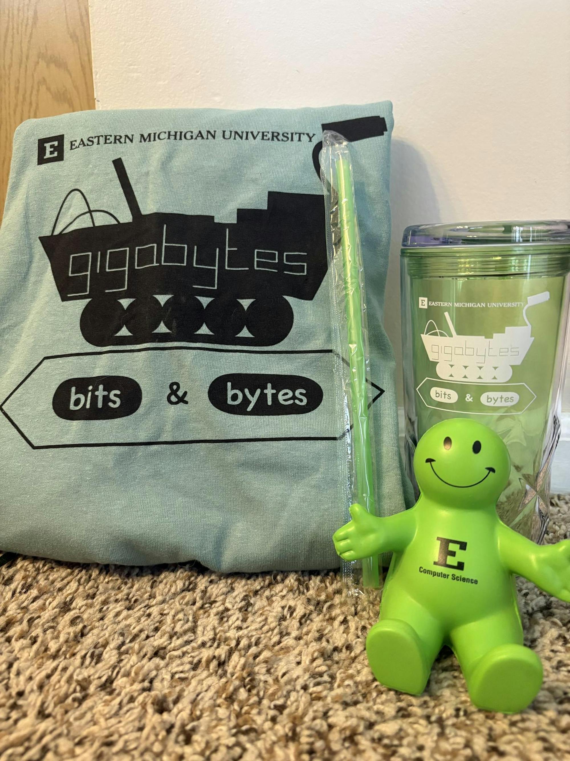 Swag items from the 2025 Bits and Bytes camp, including a shirt, water bottle and straw, and squishy phone holder. All items are green.