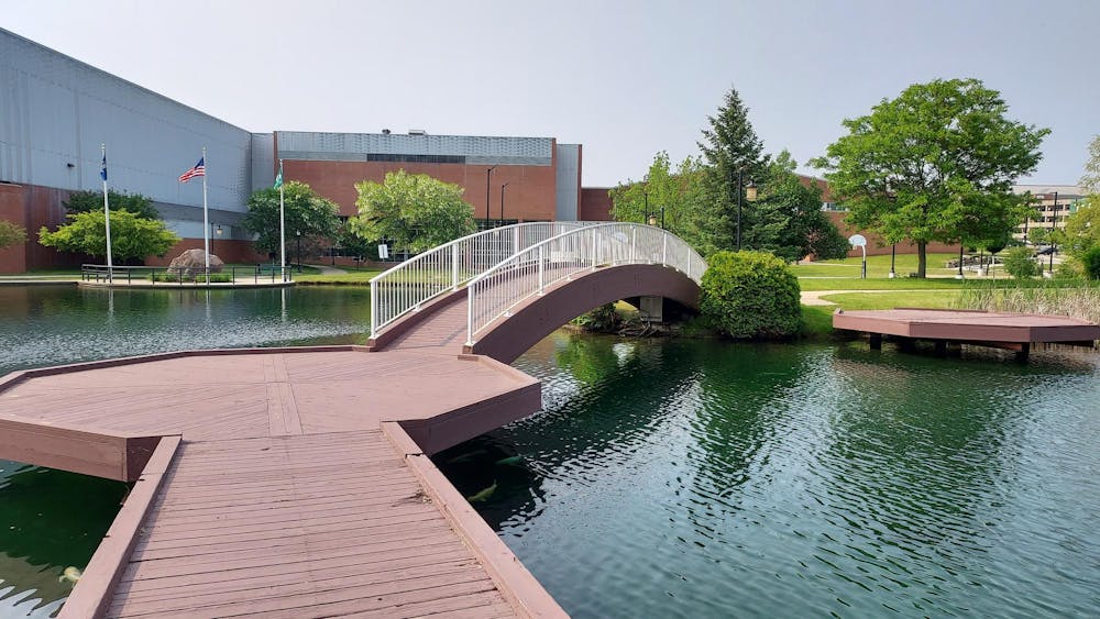 A wooden bridge over a pond with a flat platform that turns into an arch. The water underneath the bridge is a blue-green color, and the sun is shining overhead.