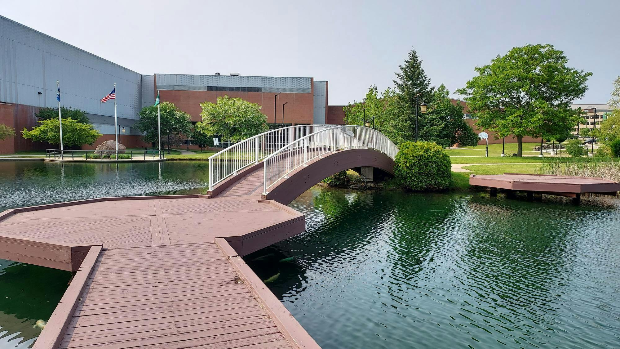 A lake view with a wooden bridge leading flat to a platform, then arched to the other side of the pond, surrounded by water.