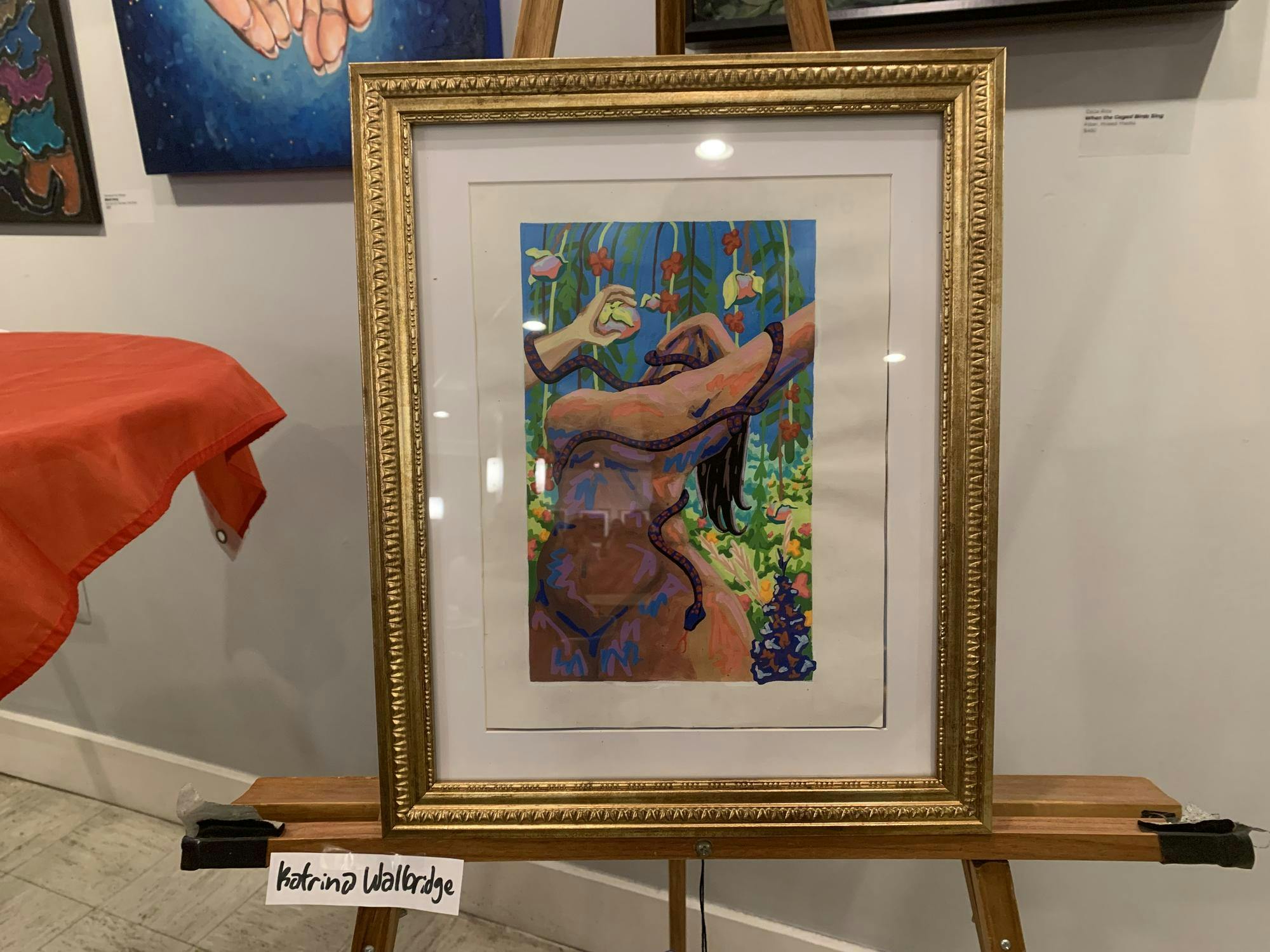 A painting inside a brown frame, showcasing a woman's nude body surrounded by green foliage and a brown snake. 