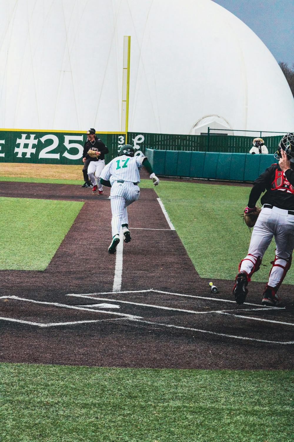 EMU baseball player, #17, in a white and green striped uniform running to first base.