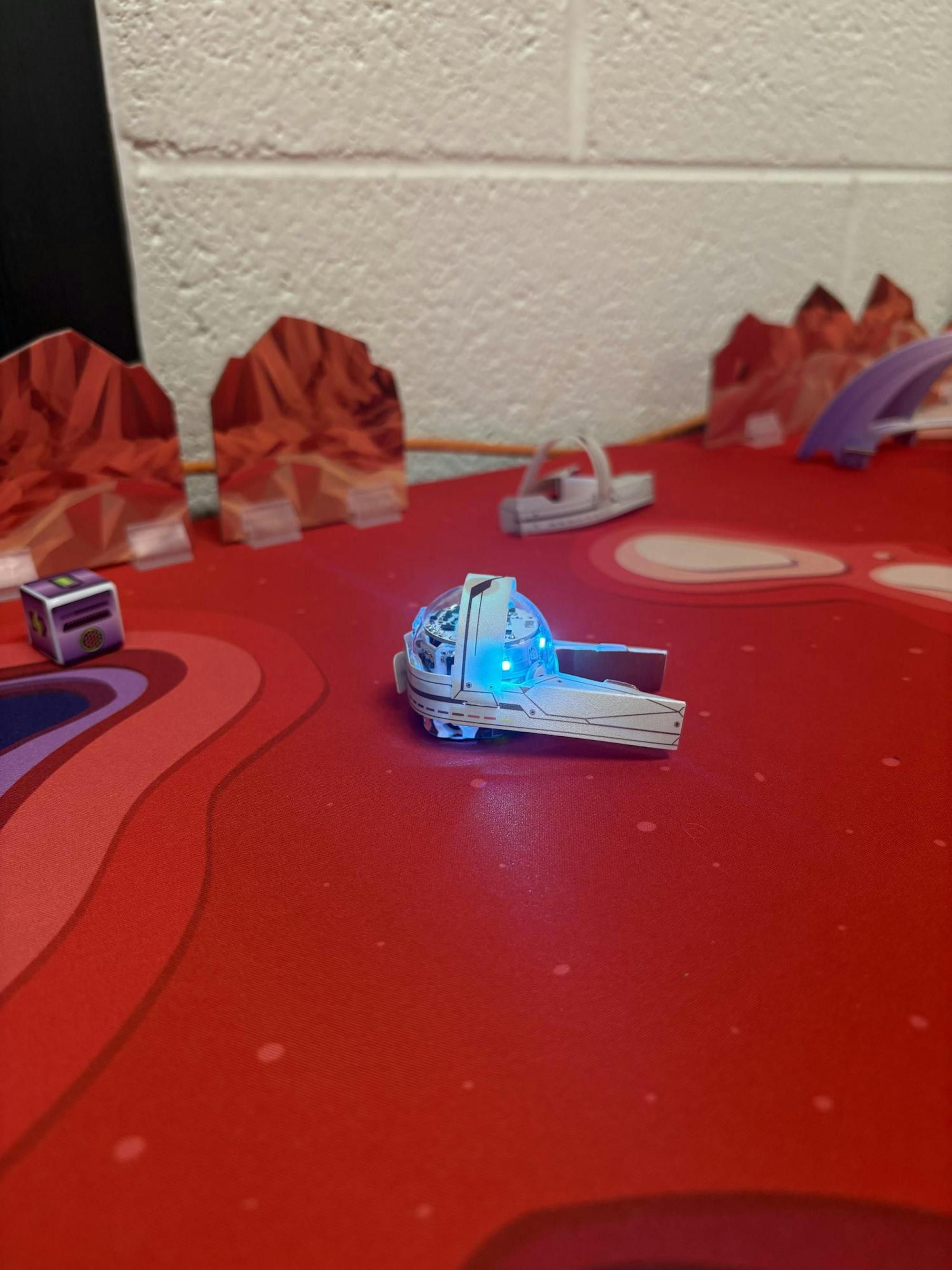 An Ozobot on a red mat carrying a paper cutout.