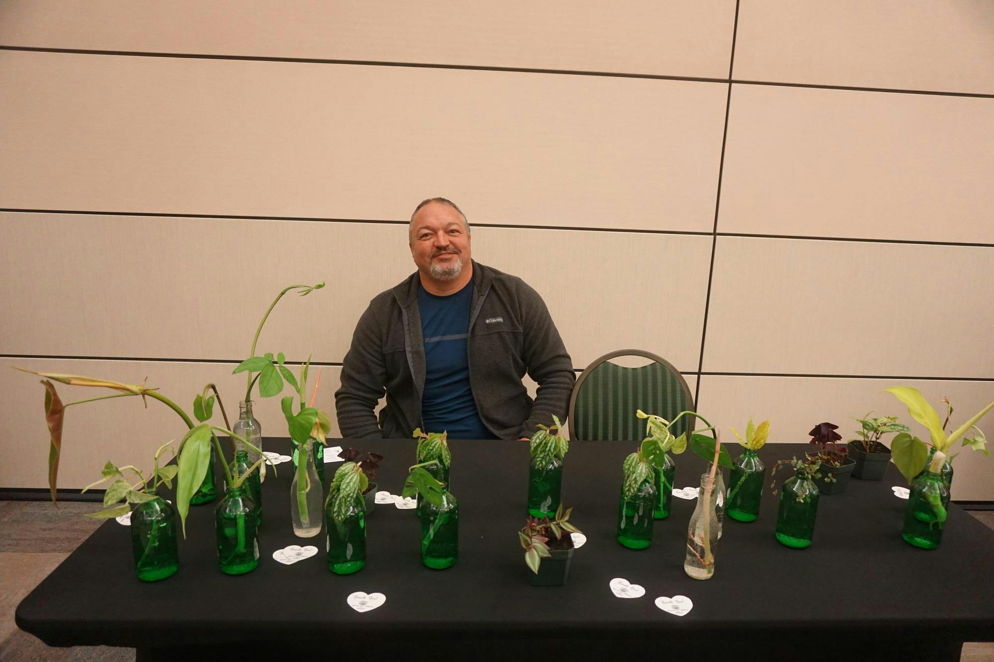 A view of Bradley Cross posing for a picture behind a table of plants grown on campus.