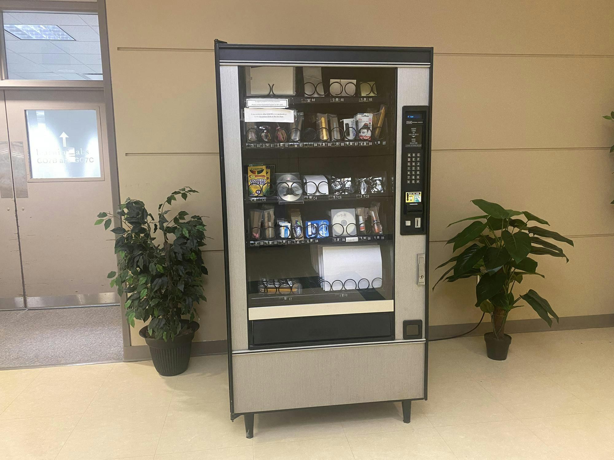 Silver and black vending machine containing school supplies like colored pencils, pens, markers, and more.