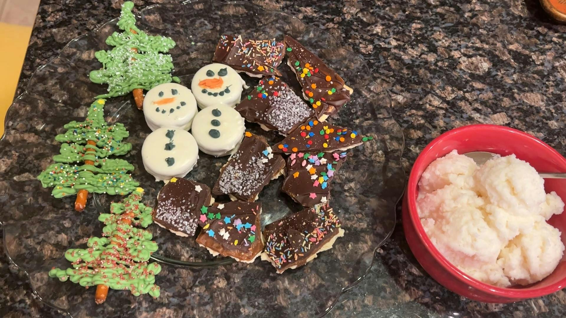 A photo of snow cream, snowmen made with two Oreos coated in white chocolate, chocolate covered toffee crackers, and Christmas trees made from pretzel sticks and green-dyed white chocolate. 