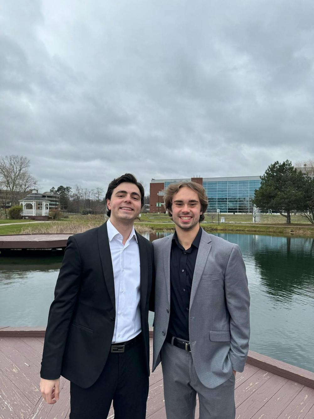 Hamzah Dajani and Jack Booth stand in front of the EMU University Pond in suits.