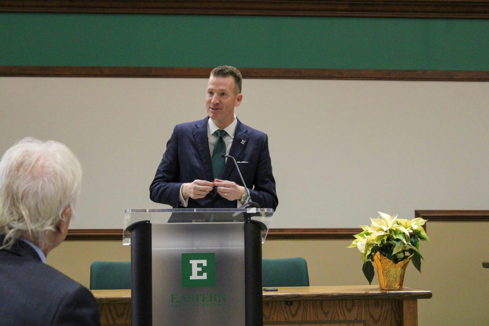 Brendan Kelly speaks from behind an EMU-branded podium.