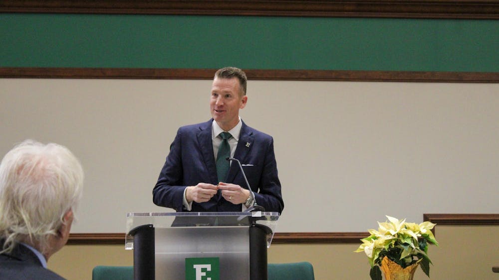 Brendan Kelly speaks from behind an EMU-branded podium.