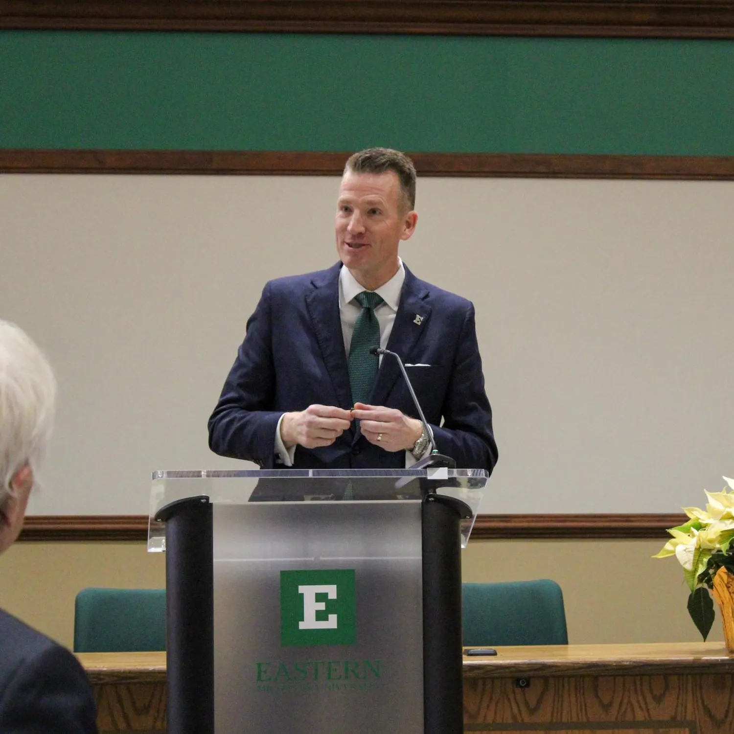 Brendan Kelly speaks from behind an EMU-branded podium.