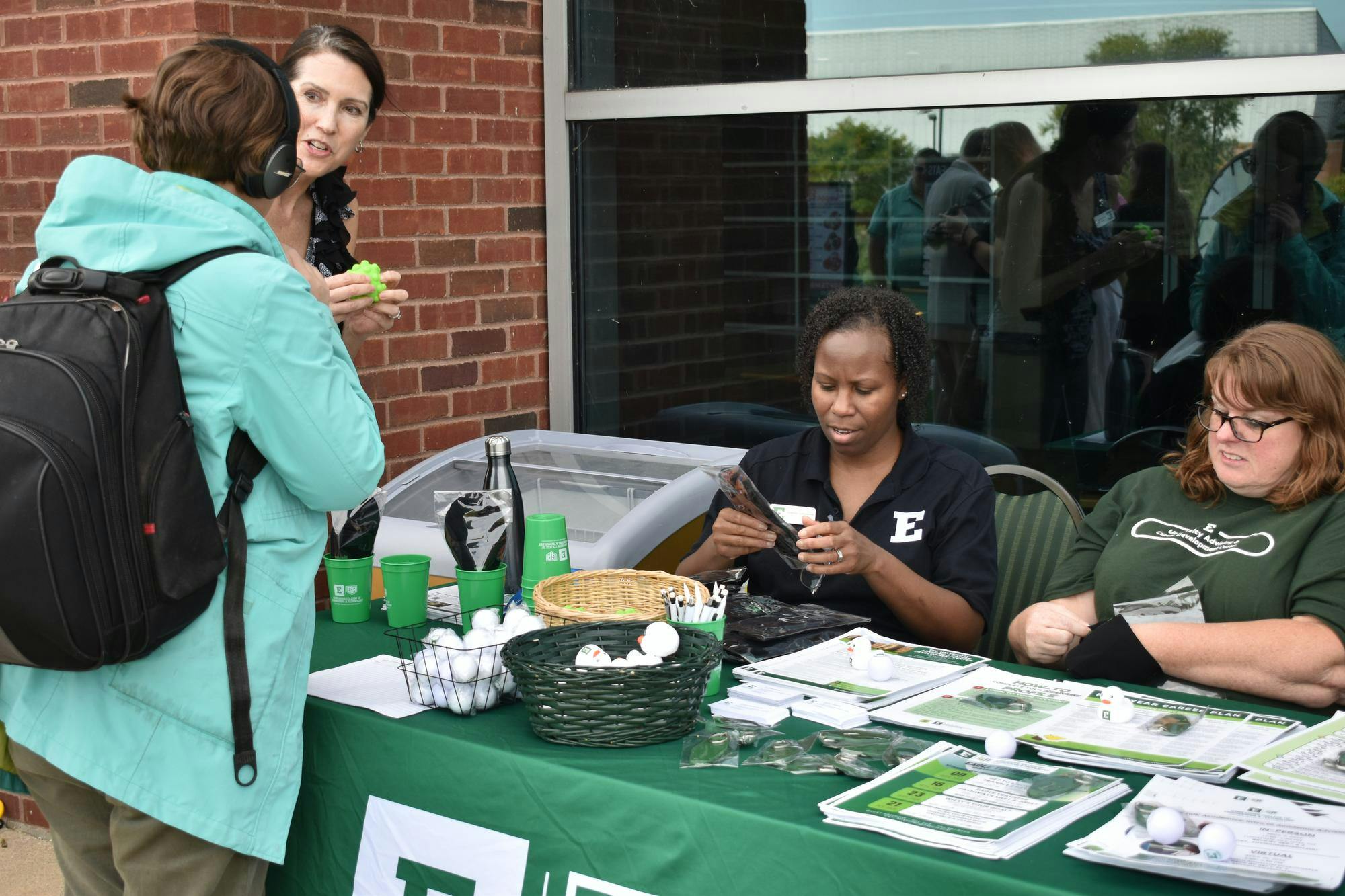 Two University Advising center employees sit at their table as two interested attendees grab items and engage in conversation. 