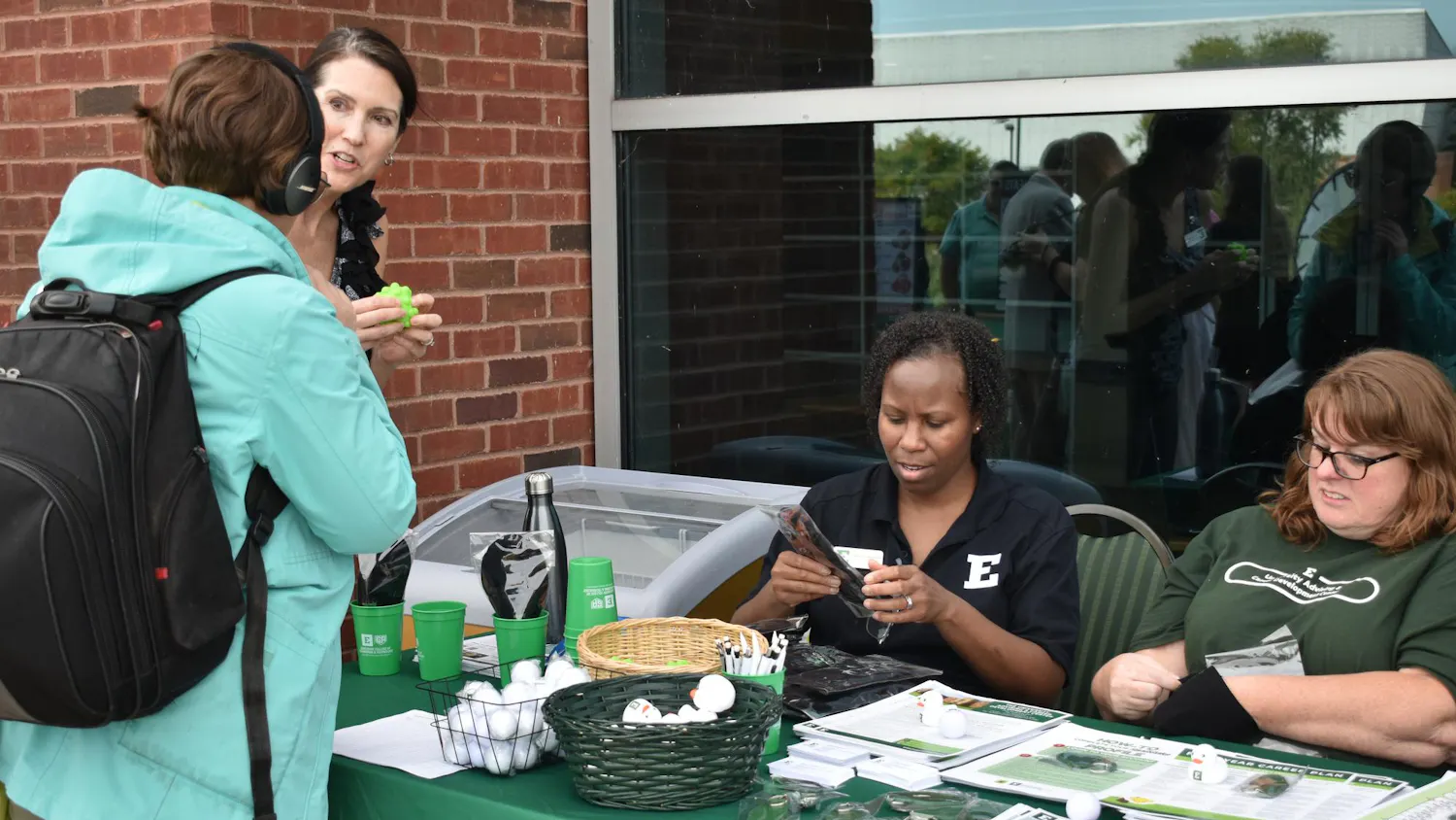 Two University Advising center employees sit at their table as two interested attendees grab items and engage in conversation.