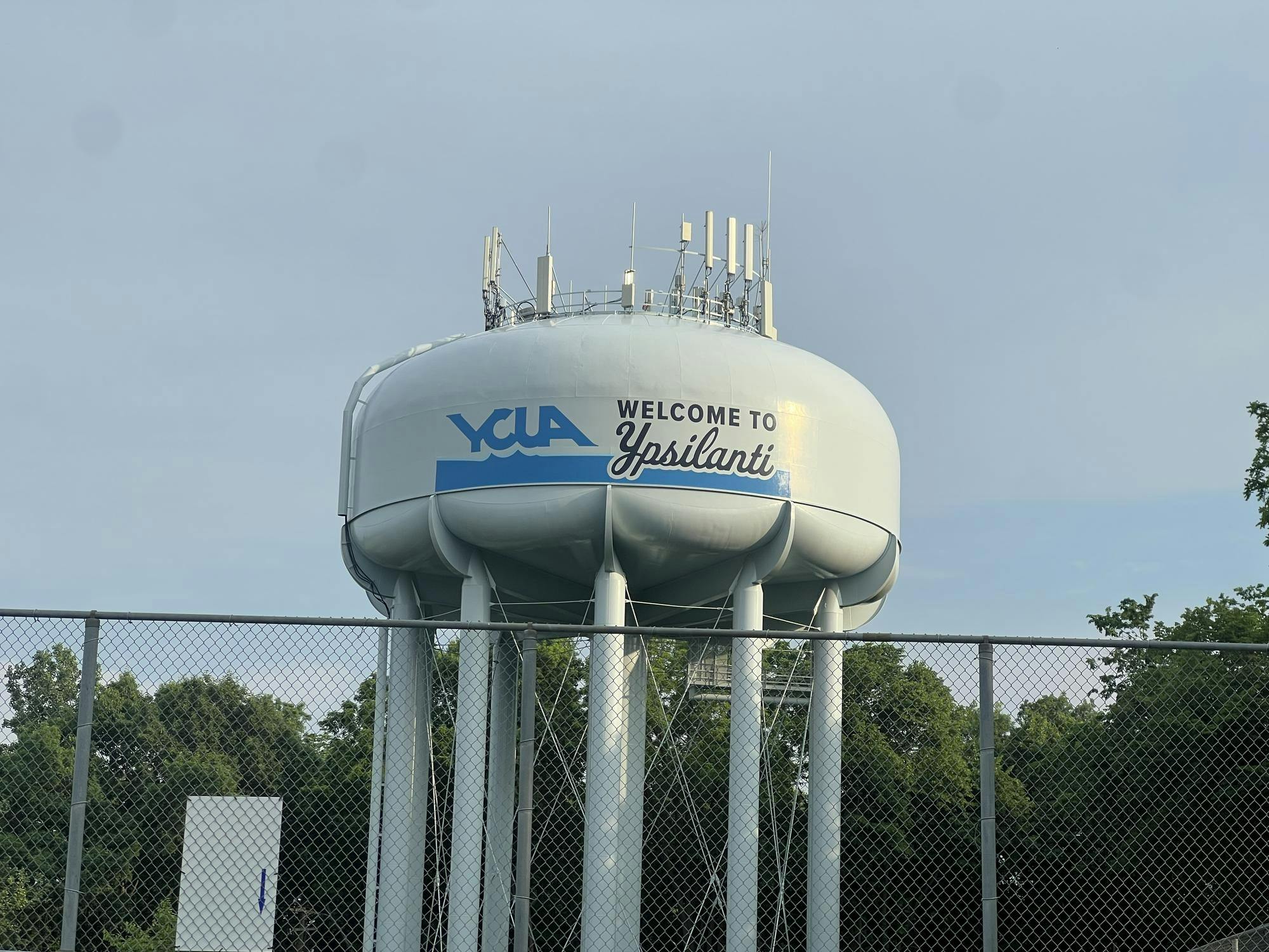 A large water tower that has the Ypsilanti Community Utilities Authority logo says "Welcome to Ypsilanti" and stands behind a fence.