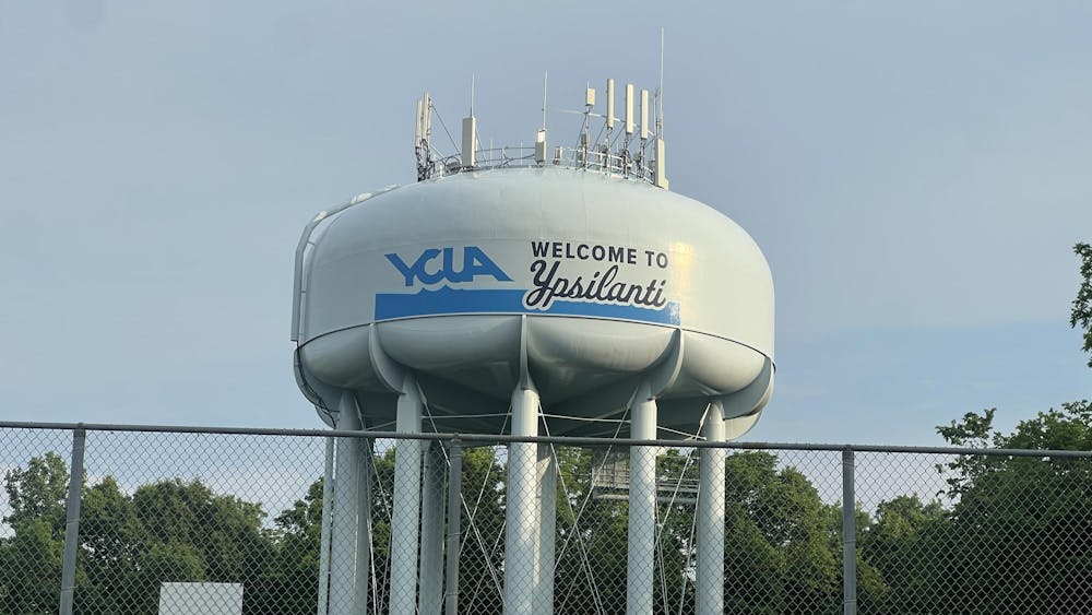 A large water tower that has the Ypsilanti Community Utilities Authority logo says "Welcome to Ypsilanti" and stands behind a fence.