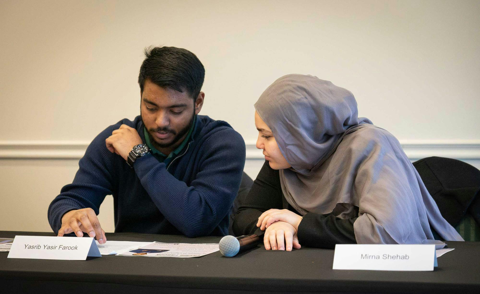 Yasrib Farook and Mirna Shehab sit at a table and look at paper materials during the forum.