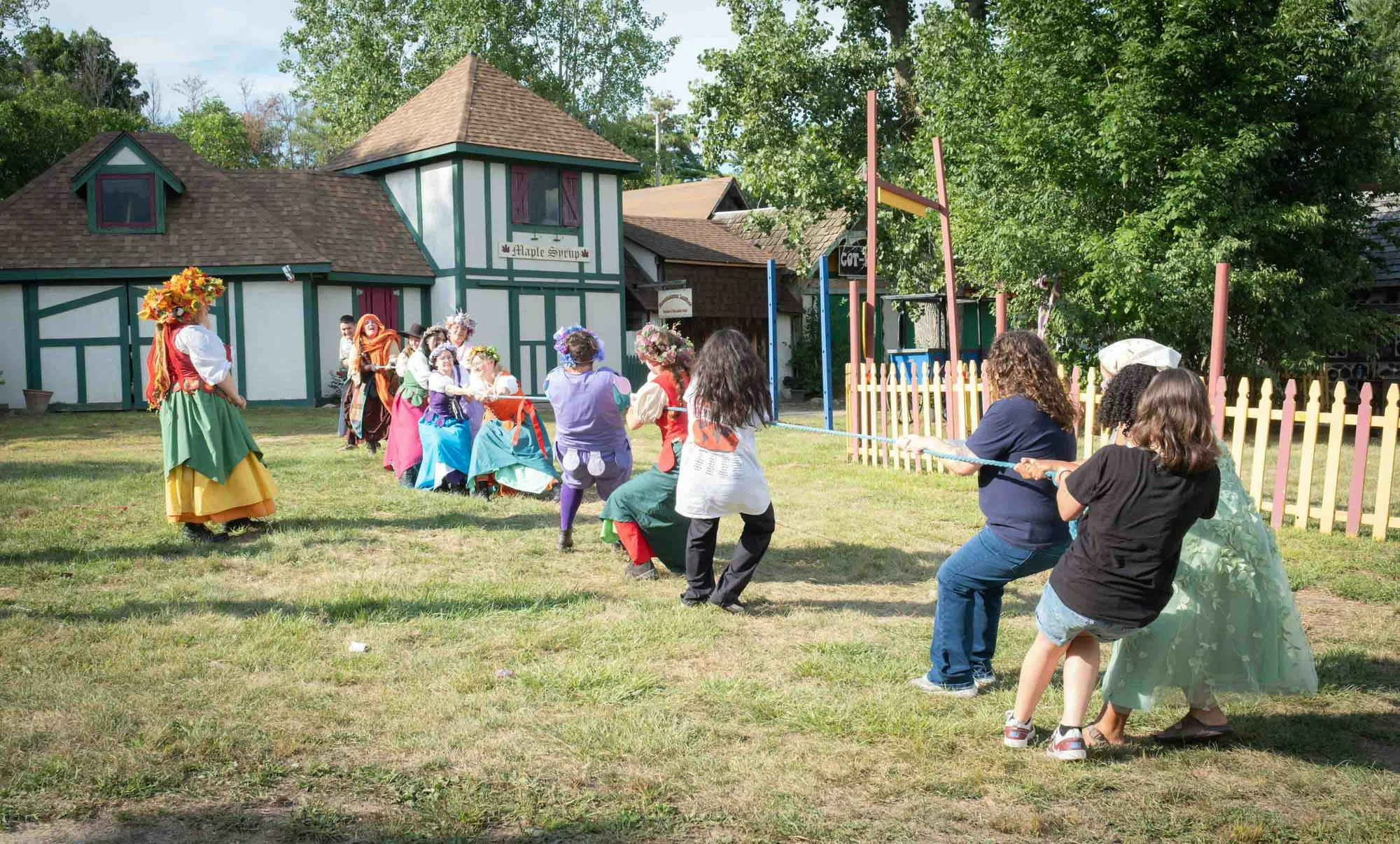 Guests and cast members pull on either side of the rope outdoors, some dressed in renaissance-themed outfits.