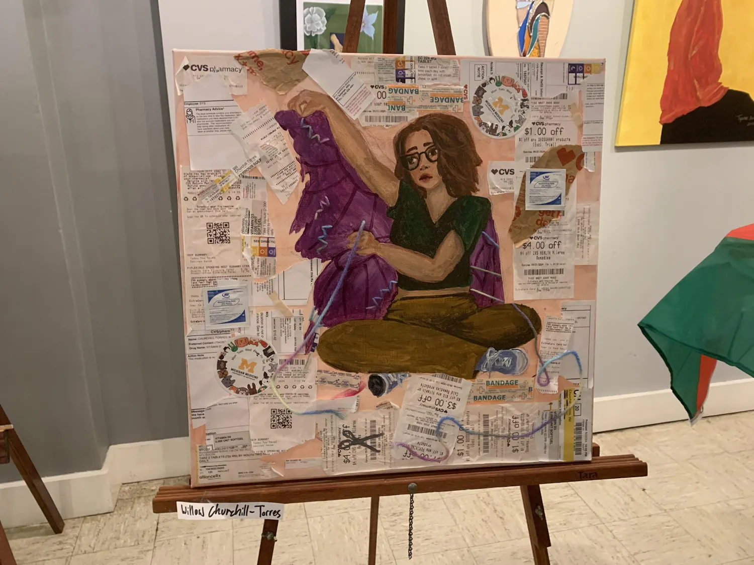 A person with glasses sits in the middle of a painting, surrounded by receipts from medical providers and pharmacy's.
