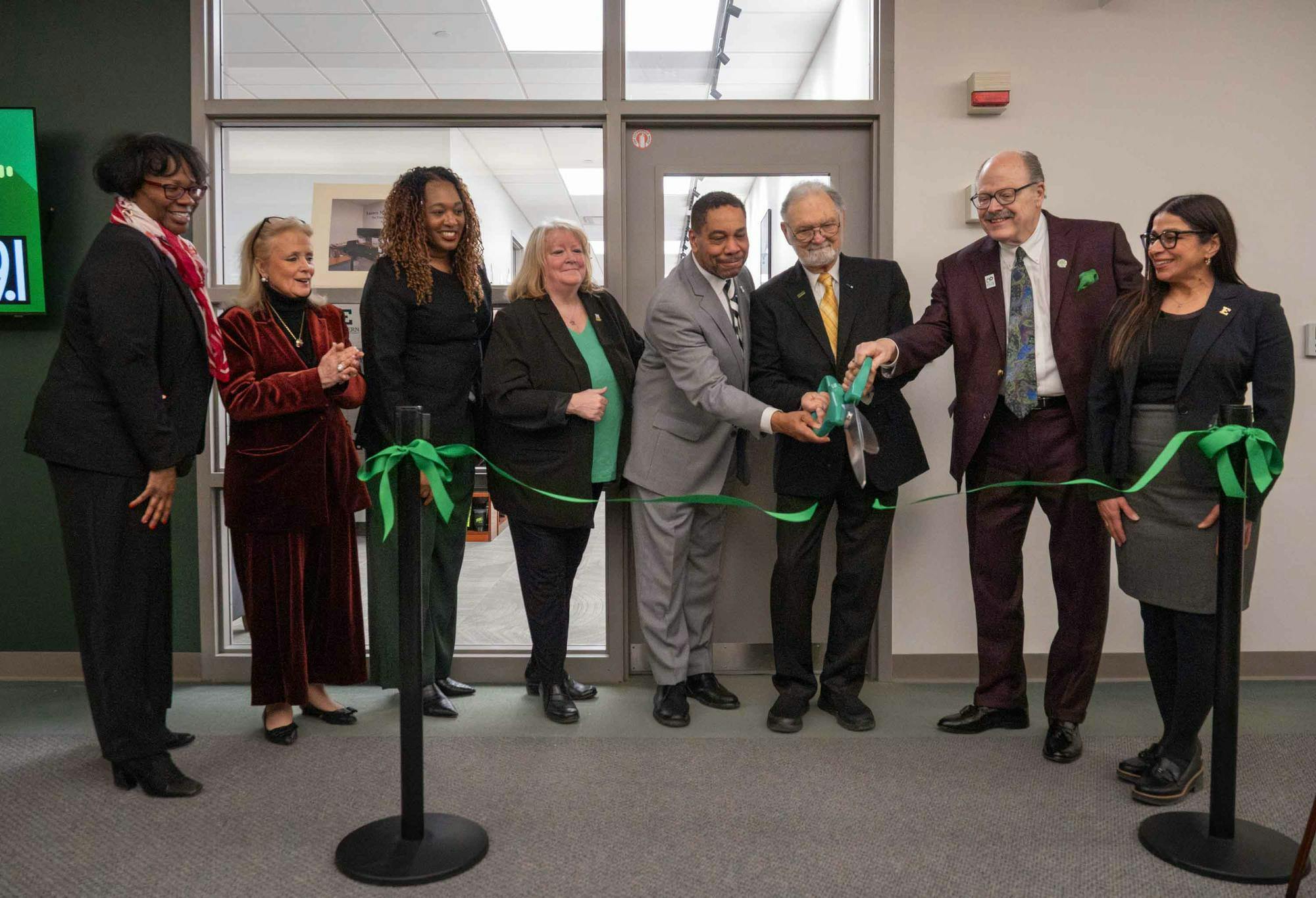 People clap and smile as Nate Ford, Art Timko, and James Smith hold oversized scissors and cut the green ribbon.
