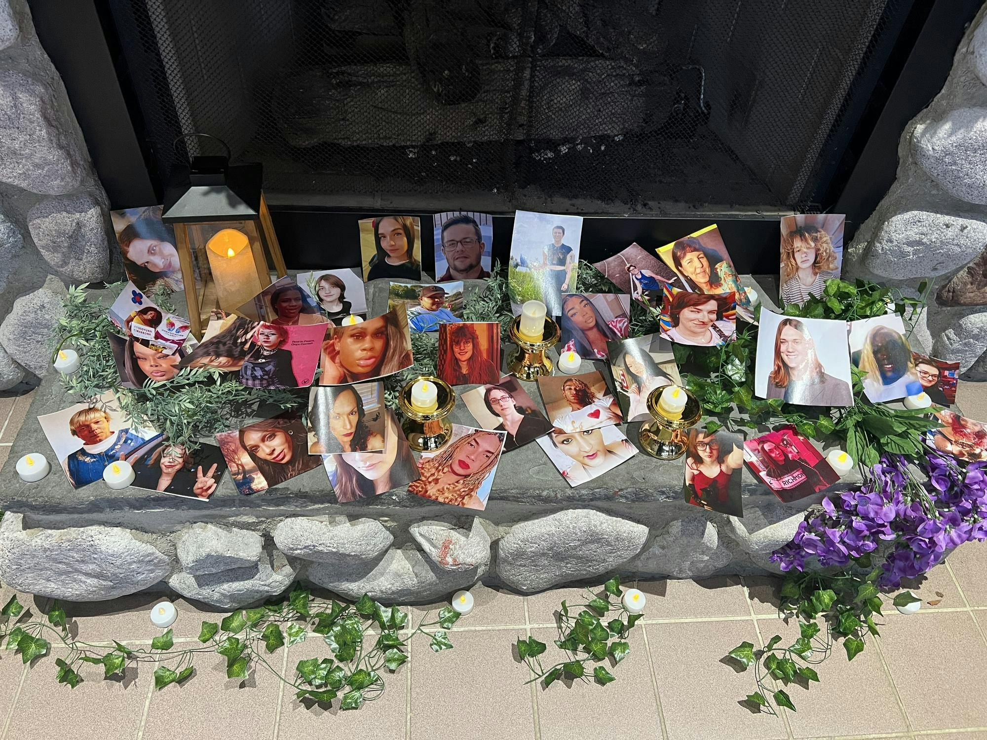 Photos of the transgender lives lost in 2024-25 adorn a stone fireplace along with LED candles and plants.