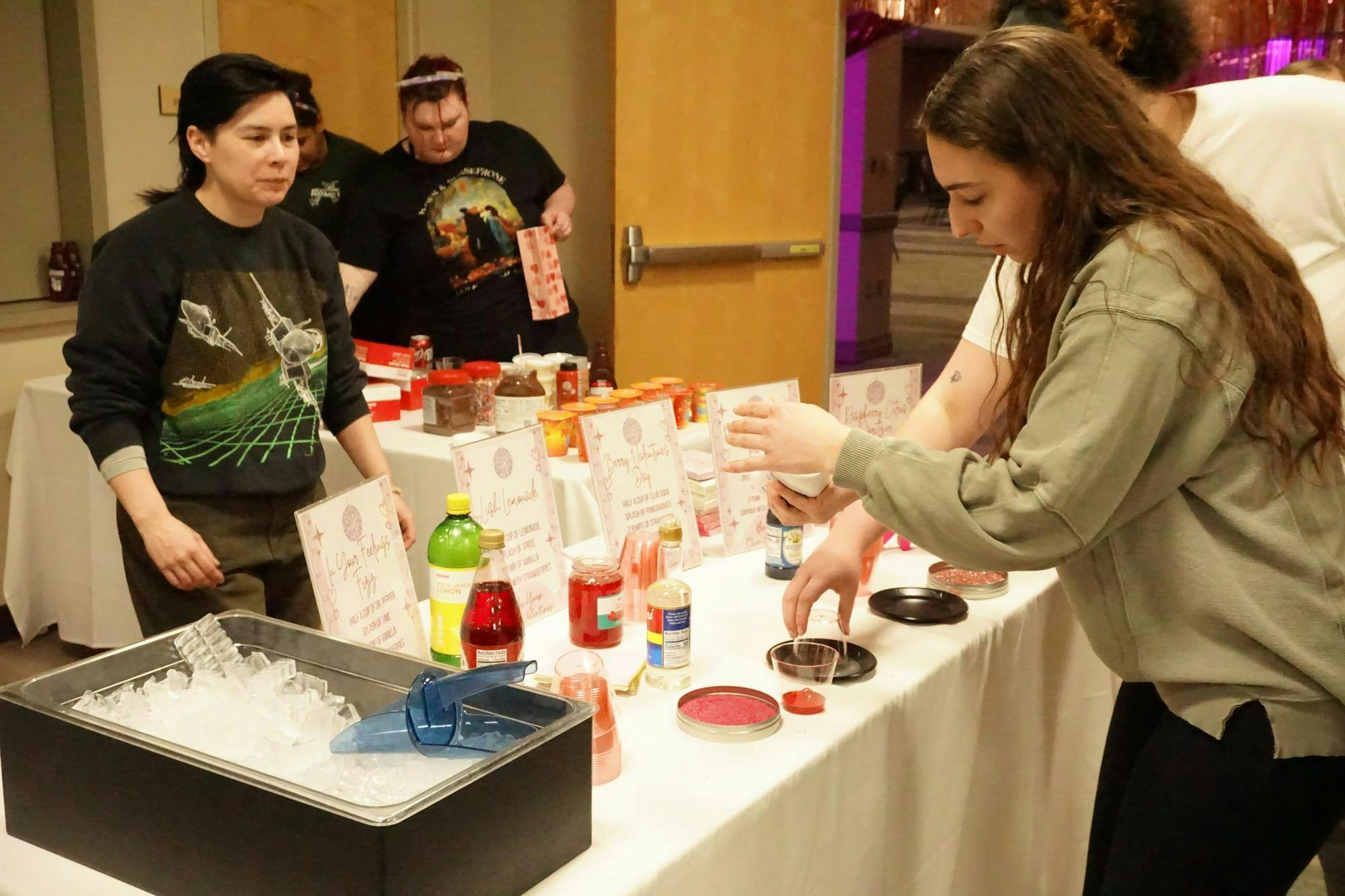 A view of students making their own mocktails with pink sugar rims and various juices and syrups.
