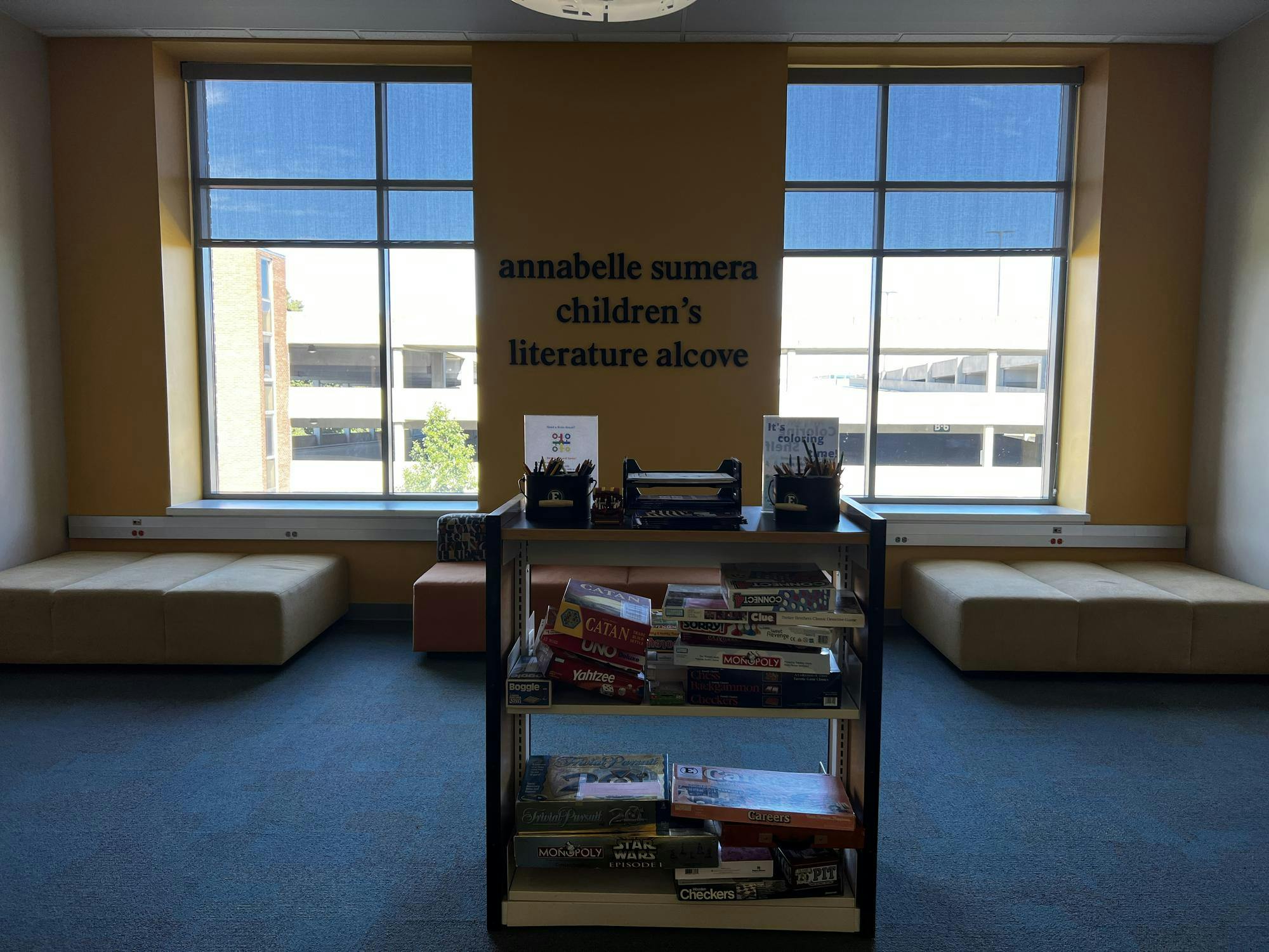 A moderately-sized alcove with two large windows and a rack of board games in the center. 