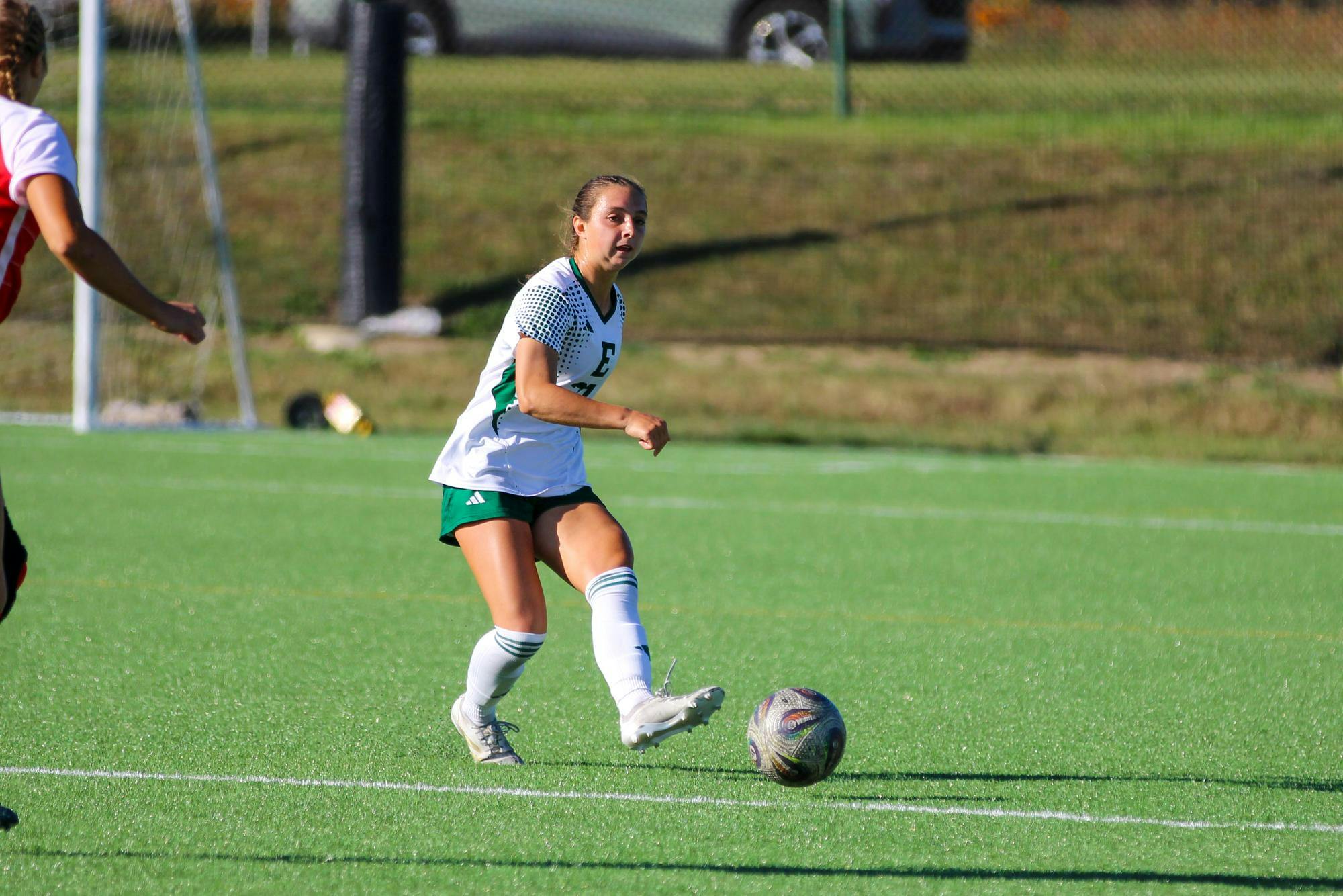 EMU player, in a white jersey, passing the ball to a teammate outside the frame