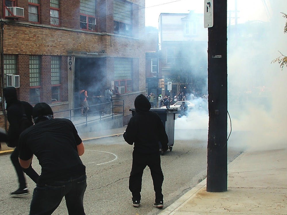 Black clad protesters heave a dumpster at riot police in response to the tear gassing of journalists, other protesters and bystanders.