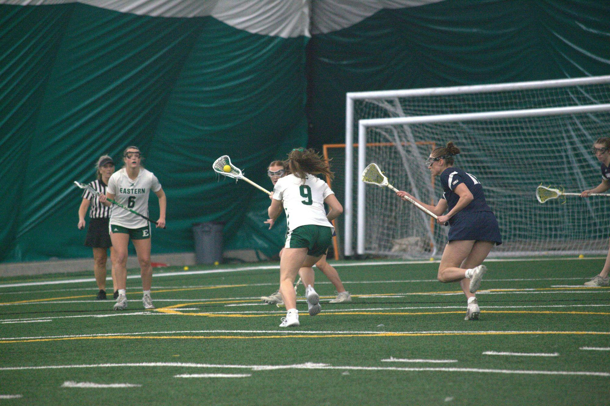 A women's lacrosse player with a ball in the pocket of their lacrosse stick dodges opposing team players on field.