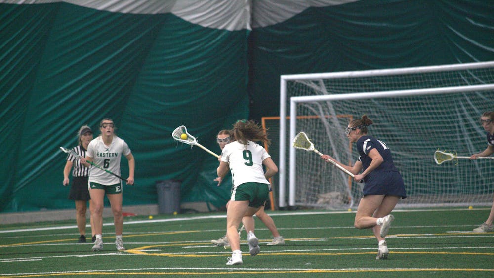 A women's lacrosse player with a ball in the pocket of their lacrosse stick dodges opposing team players on field.