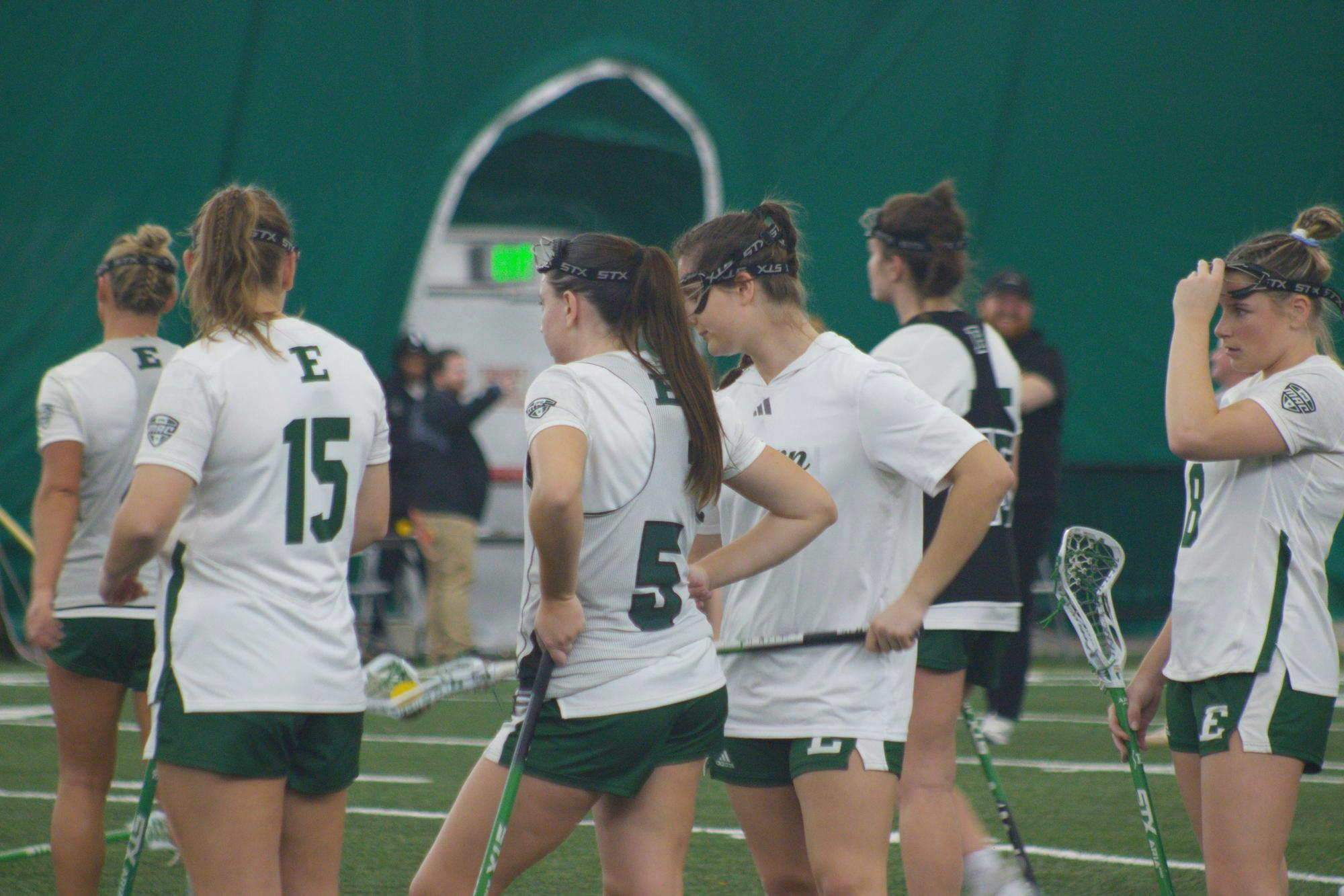 6 Eastern Michigan Lacrosse players in white jerseys stand waiting for the next play. 