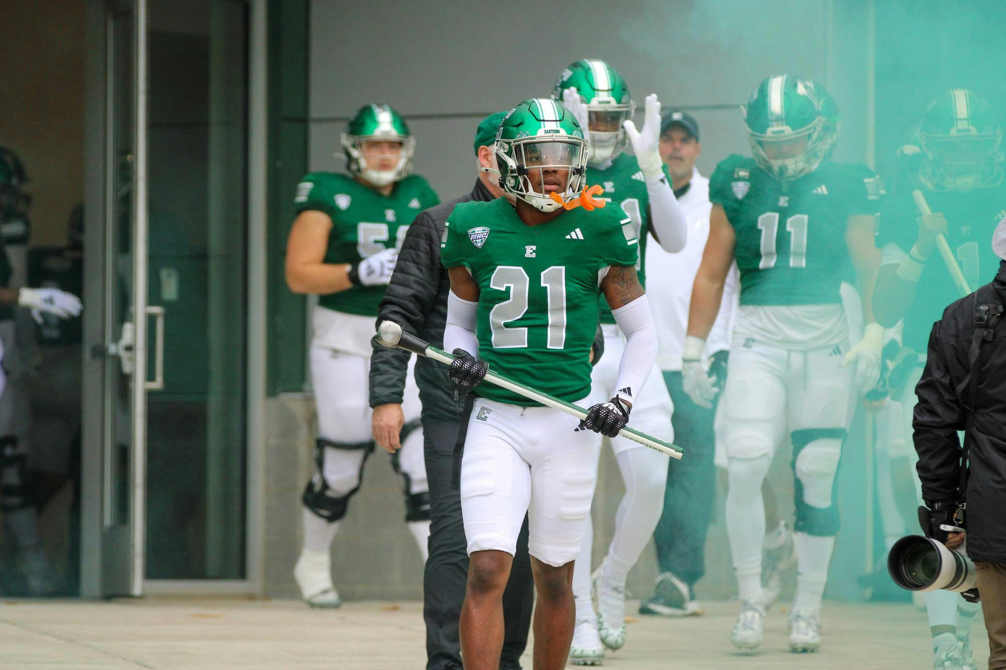#21, in a green jersey, walks up to the concrete wall holding a sledgehammer