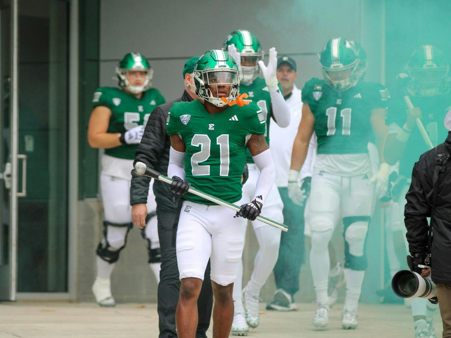 #21, in a green jersey, walks up to the concrete wall holding a sledgehammer