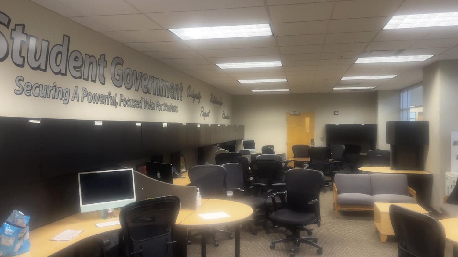 An office space with several chairs, desks and computers. Lettering on the wall says "Student Government" and "Securing A Powerful, Focused Voice For Students."