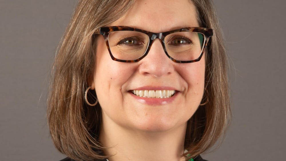 Headshot of Jeanette Zalba from the shoulders up, wearing a green blouse and black suit jacket with an EMU pin affixed to the collar.