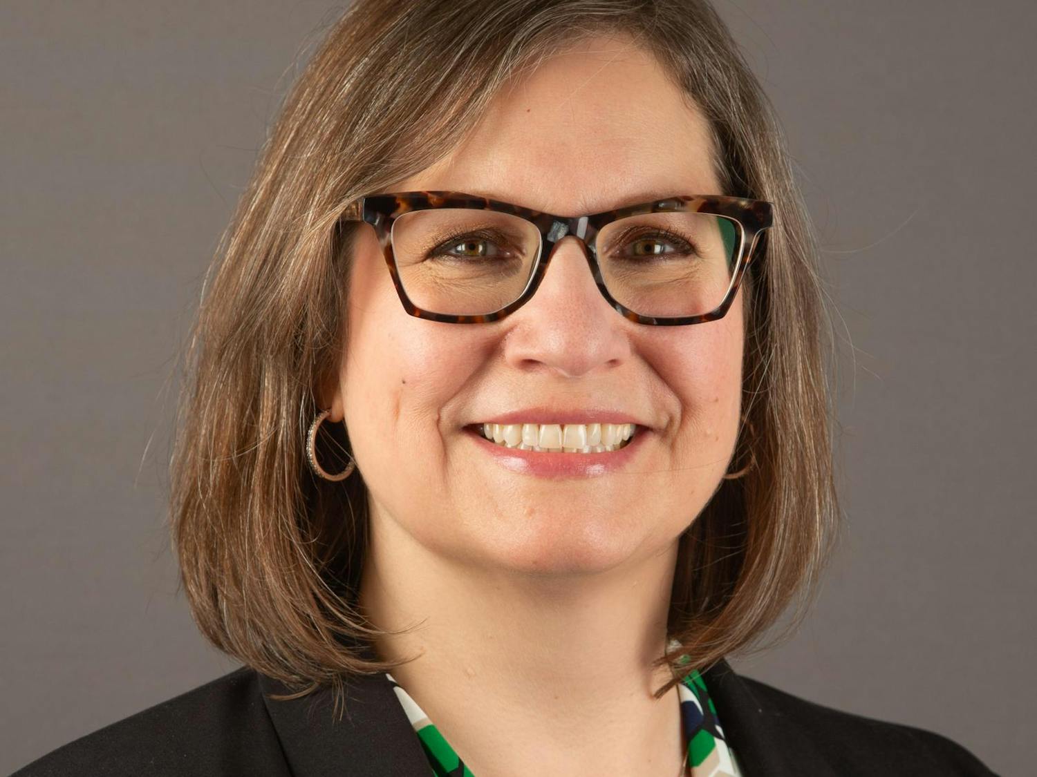 Headshot of Jeanette Zalba from the shoulders up, wearing a green blouse and black suit jacket with an EMU pin affixed to the collar.