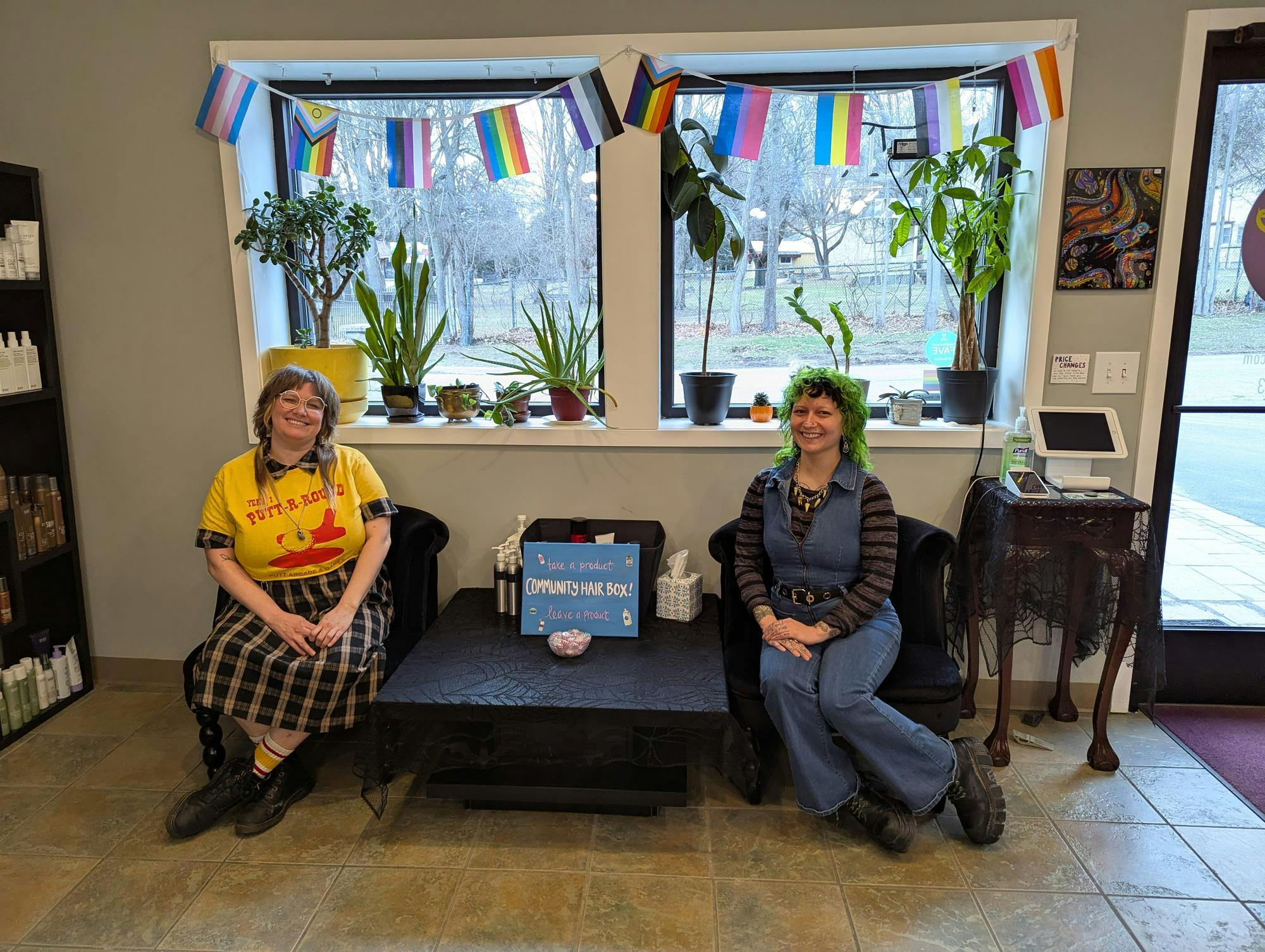Two people sitting in chairs with pride flags behind them.