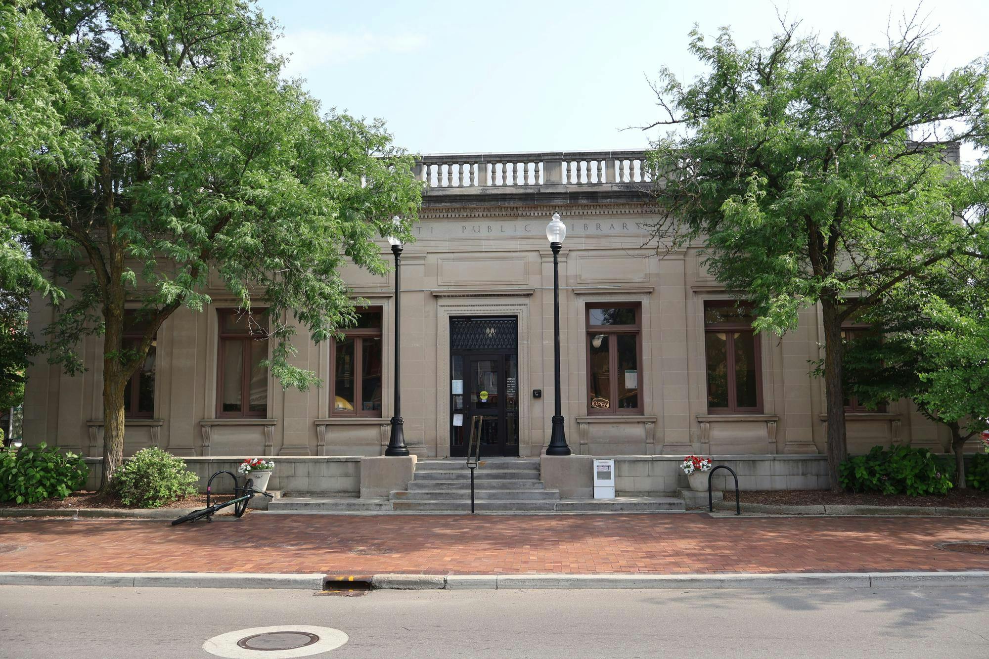 A stone builiding with Ypsilanti Public Library carved at the top surrounded by trees.