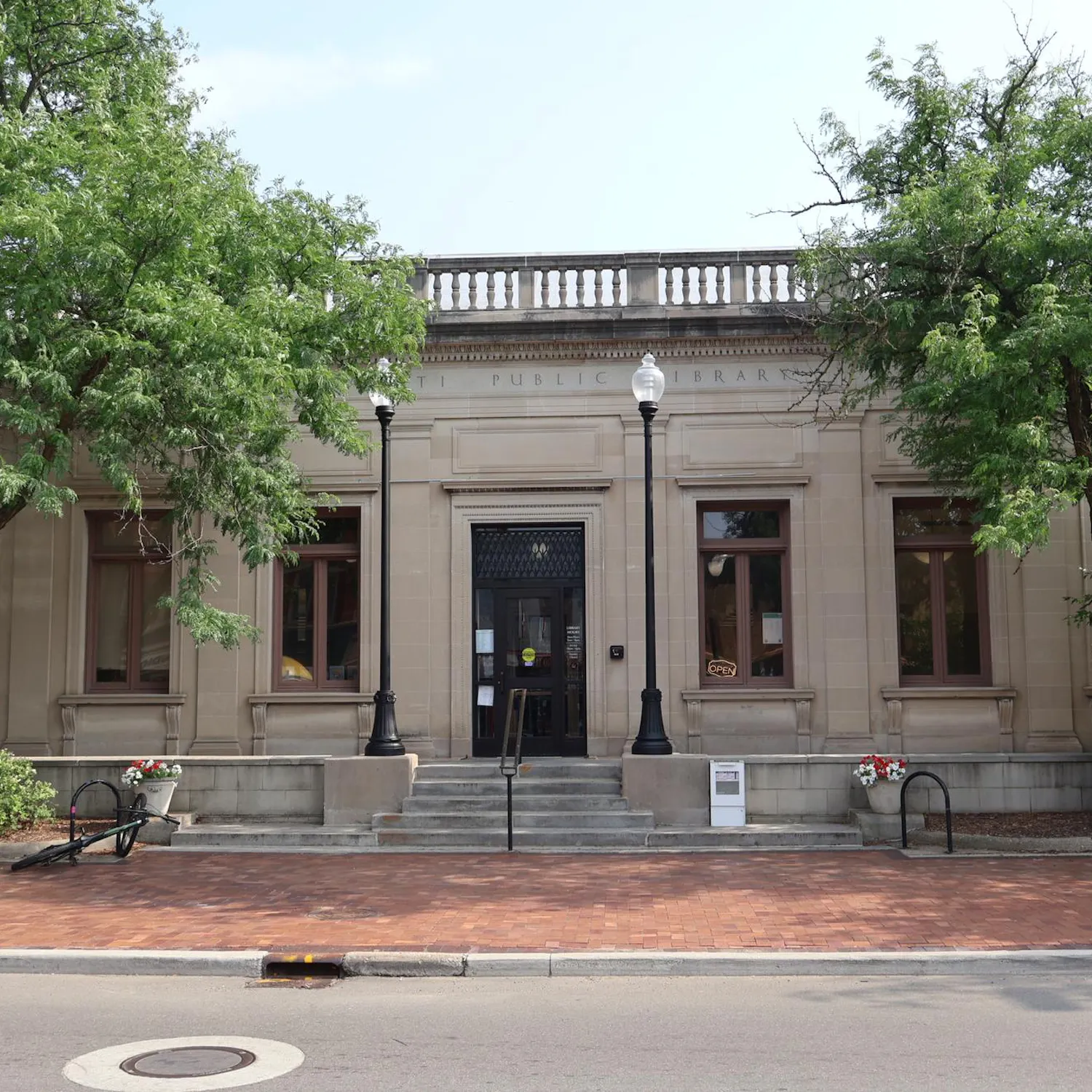 A stone builiding with Ypsilanti Public Library carved at the top surrounded by trees.