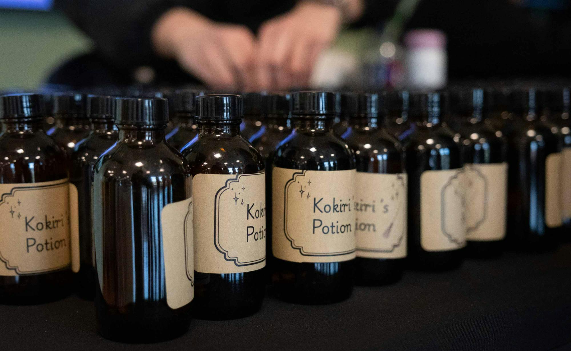 Cose-up of many small glass bottles displayed together on a black table. The bottles are labeled "Kokiri's Potion."