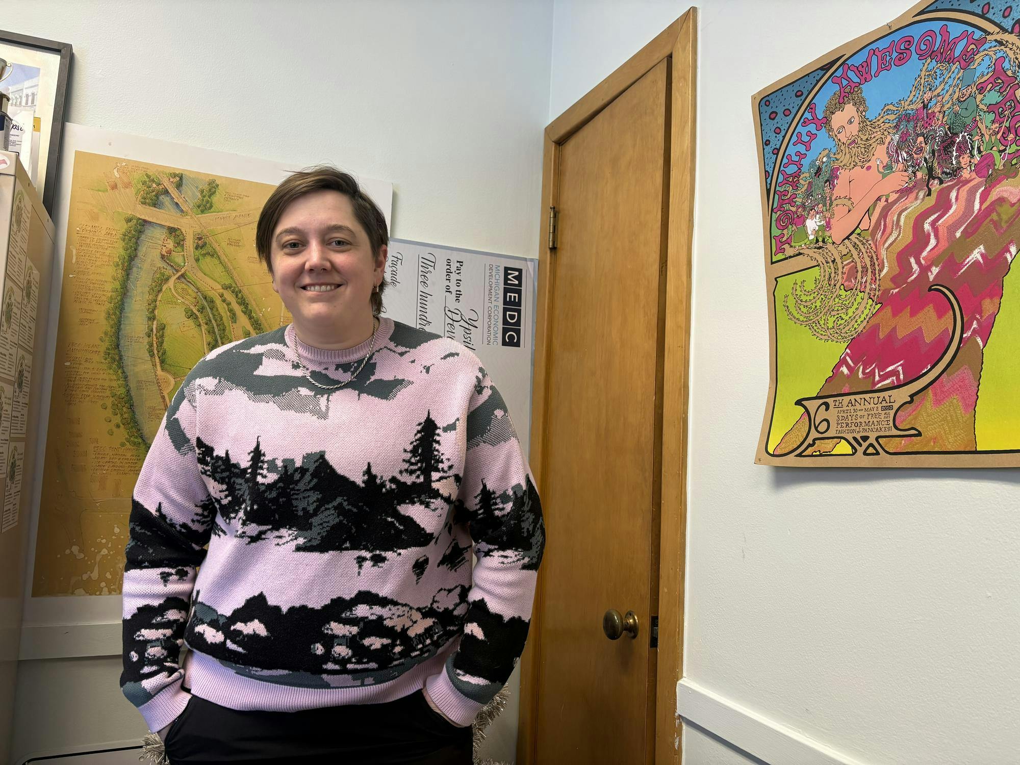 Eliza Jekabson stands in an office smiling; in the background there are colorful posters.