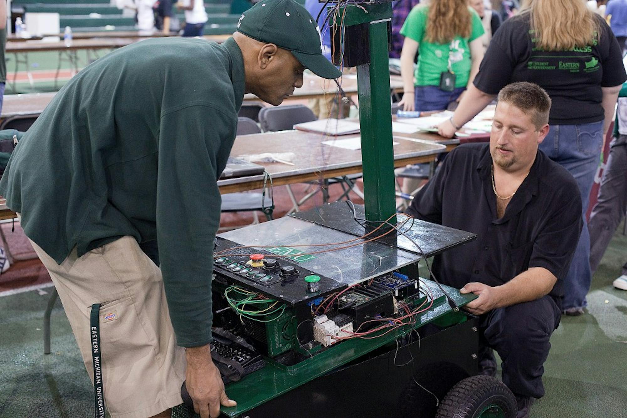 Nathan Jones (left), president of the Robotics Society at EMU, lifts the electronics and top of the new robot with some help from member Corey Horvath.  The robot was present at this year's Fajita Fest in Bowen Field House.
