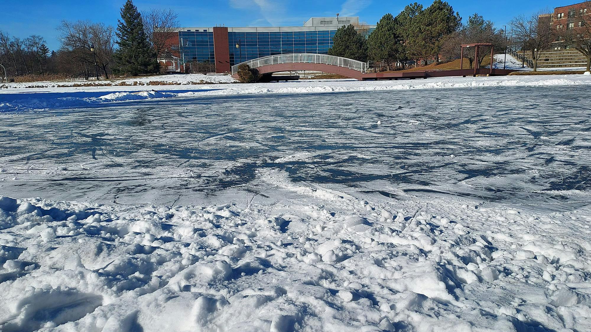 At the top of the picture, the wooden bridge is used as a pass above the frozen pond, which is on the bottom side of the photo.