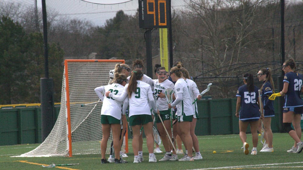Women's lacrosse players huddle outdoors on a lacrosse field near a goal.