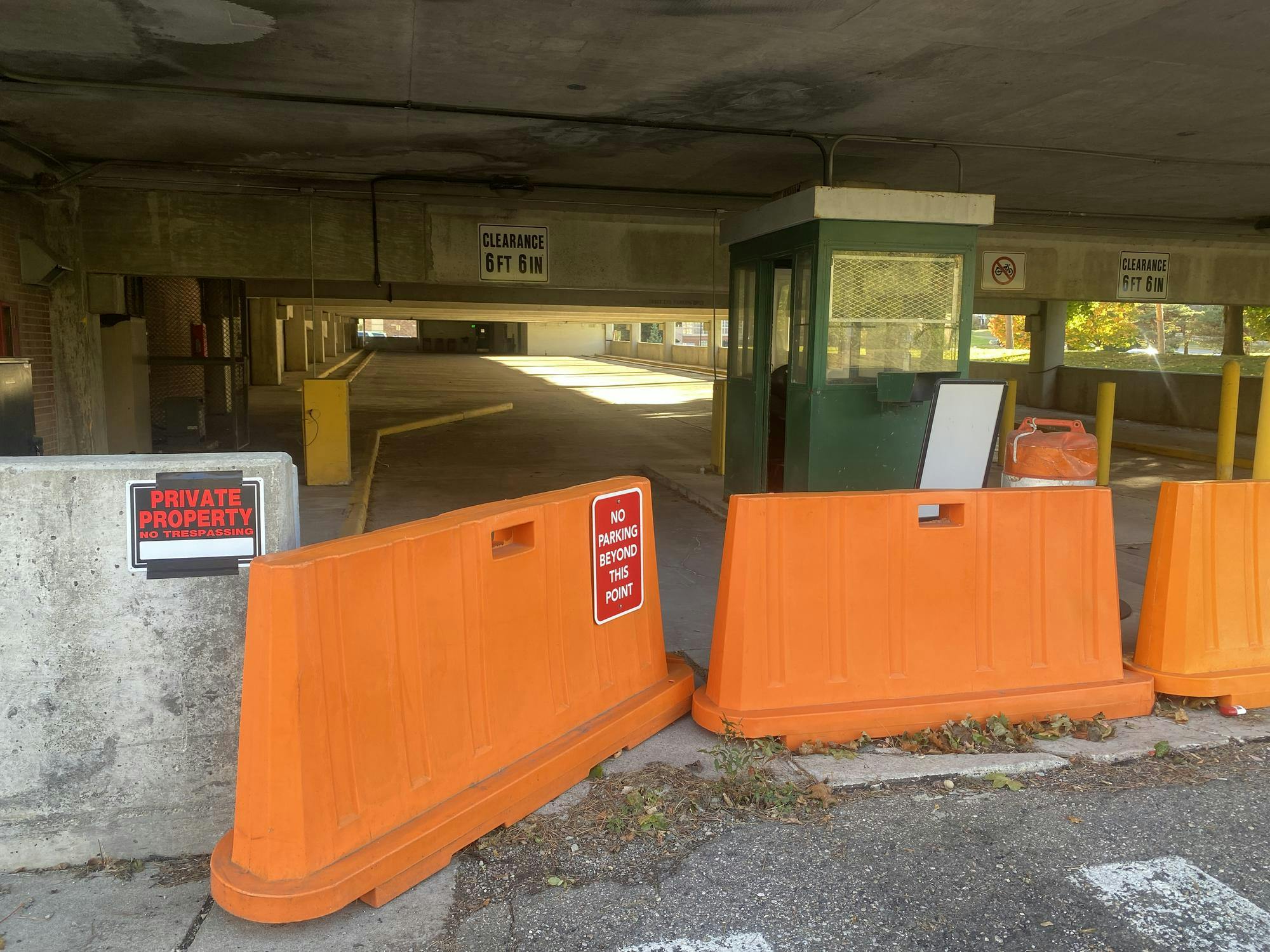 Close-up of the main entrance of the closed parking structure on EMU campus. Orange barriers block the entrance, and signs read "Private property, no trespassing" and "No parking beyond this point."
