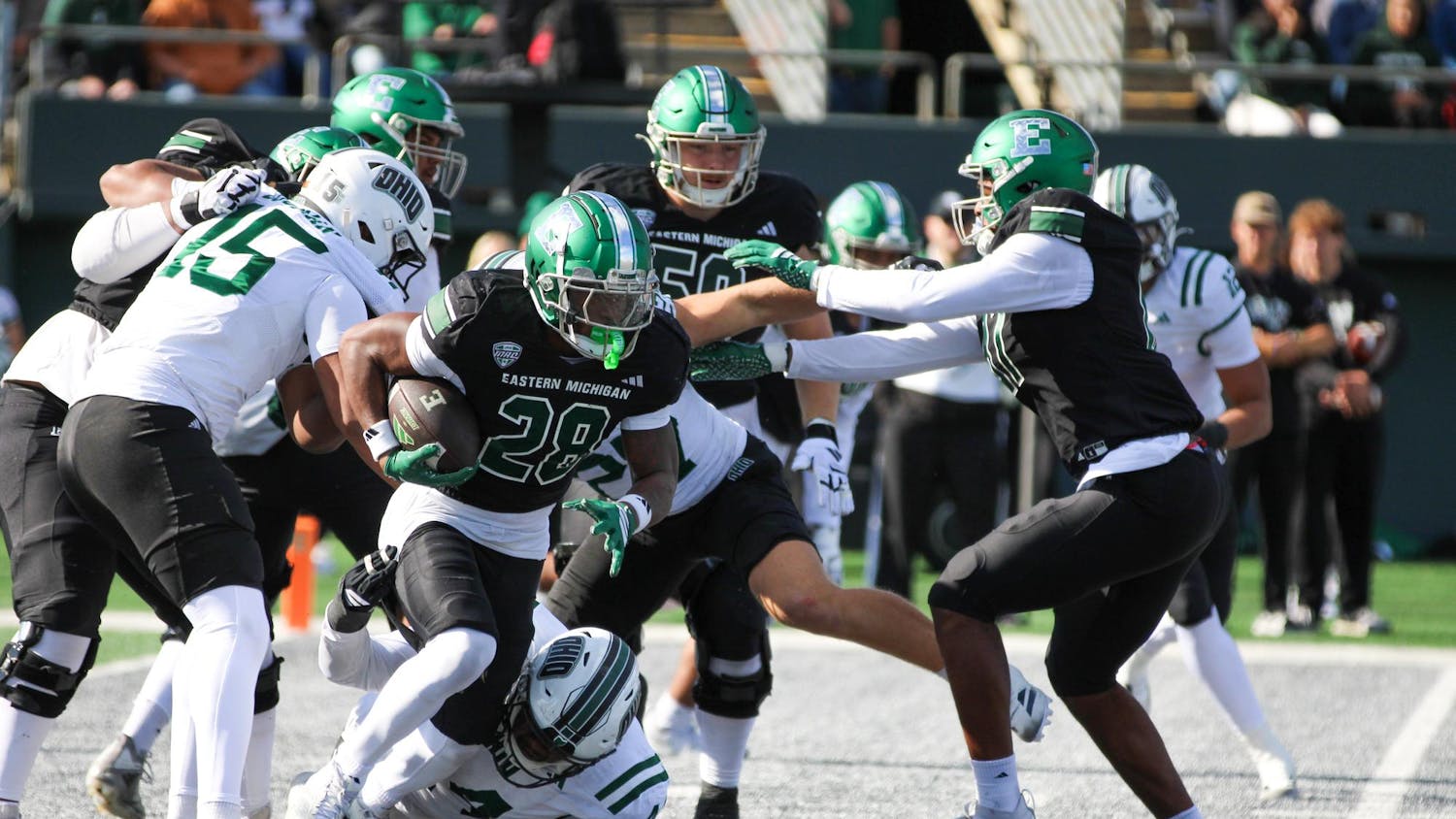EMU's football player, #28, in a black jersey, pushes through Ohio's defensive line, all in white jerseys