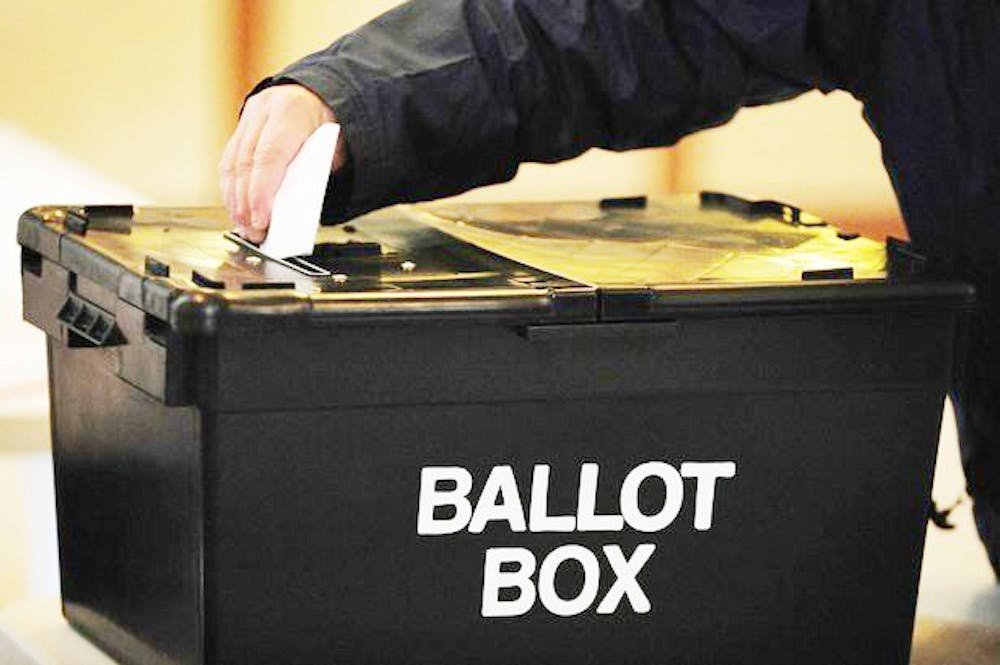 A-voter-placing-a-ballot-paper-in-the-ballot-box-at-the-polling-station-at-Market-Hall-in-Swadlincote-Derbyshire.jpg