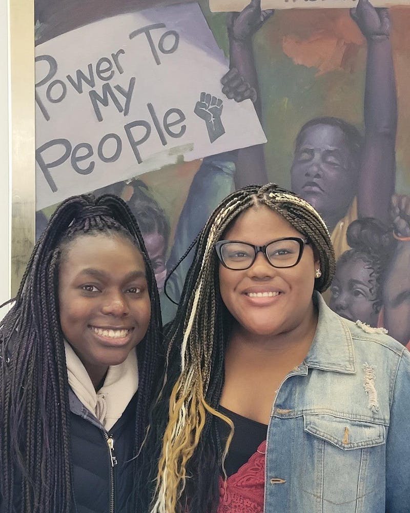 Freshmen Vagi Trotter and Briona Graham stand in front of an empowerment sign inside of the NAAMCC.