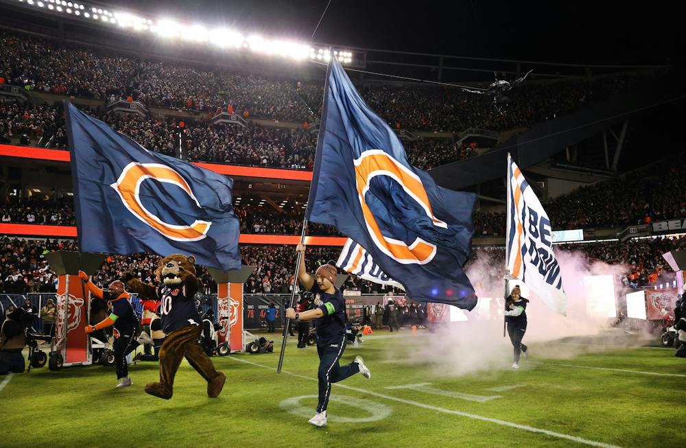 <p>Workers carrying Bears team flags run onto the field before players introductions ahead of the NFC wild-card game against the Packers on Jan. 10, 2026, at Soldier Field. (Chris Sweda/Chicago Tribune/Tribune Content Agency)</p>