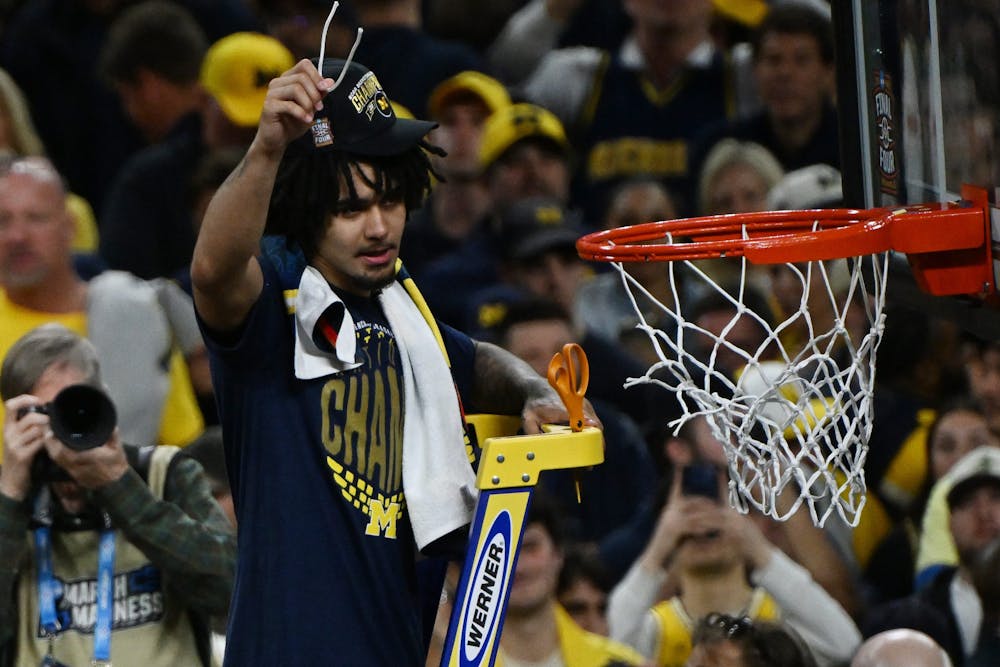 Michigan's Elliot Cadeau cuts down a piece of net after beating UConn in the NCAA Final in Indianapolis, Indiana on April 6, 2026. (Daniel Mears, The Detroit News, Tribune Content Agency)