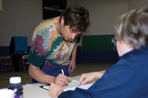 Brandon Foltz / IDSPoll worker Sally Hegeman assists Jerry Ramusach with signing in to vote Tuesday afternoon at Childs Elementary.