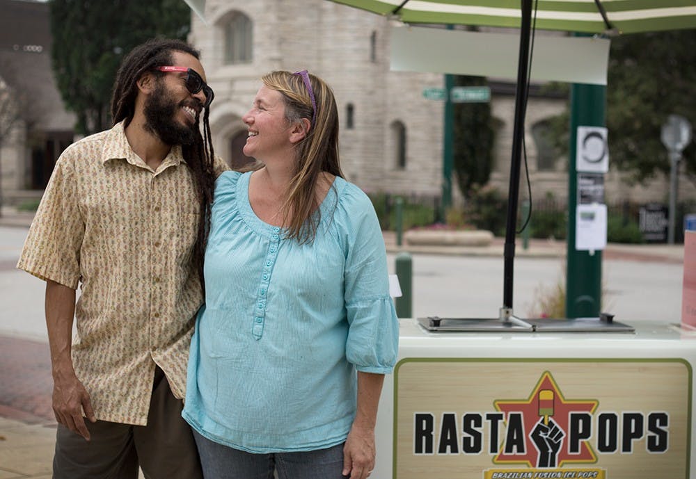 Husband and wife, Iuri Santos and Linda Lewis, pose beside their first business endeavor, Rasta Pops. The pair met while Lewis was teaching English in Brazil, Santos' homeland, and after three months decided to marry and live together in the United States. After fifteen years they have two children, Zeca, 13, and Zara, 10, and have kept a connection to Brazil through continuing traditions and now, running their Brazilian-inspired ice pops business.  